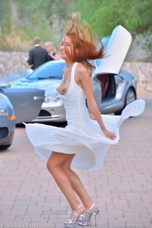 Playful minx poses on road in white dress that can barely cover her assets