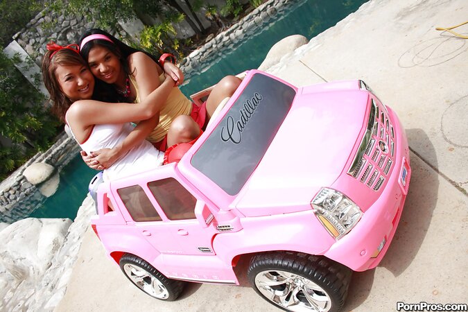 Black girl in pink headband and lesbian friend have fun by Cadillac Escalade toy