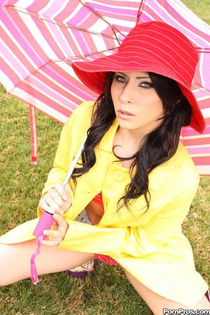 Young woman in red hat and yellow coat poses naked under an umbrella