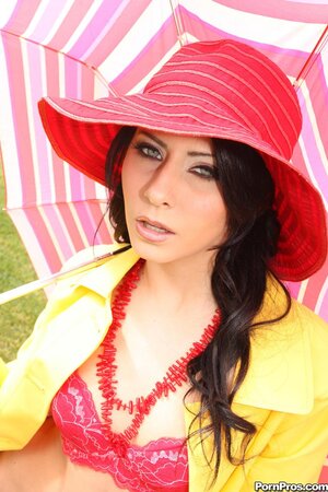 Young woman in red hat and yellow coat poses naked under an umbrella