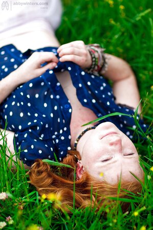 Super-pale ginger lays on the green grass and poses absolutely nude