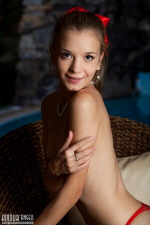 Skinny cutie with a red bow takes part in naked photo session by the pool