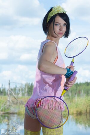 Young woman with black hair waits for partner with two rackets slowly stripping
