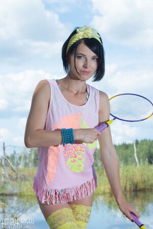 Young woman with black hair waits for partner with two rackets slowly stripping