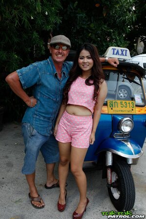 Man in flat cap and sunglasses asks Thai lovely with curly hair to pose on camera