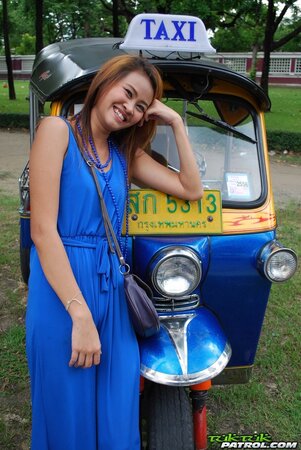 Hot female from Thailand poses in her slinky blue dress by a small taxi