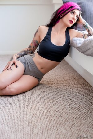Tattooed woman poses in bedroom in lingerie that accentuates her assets