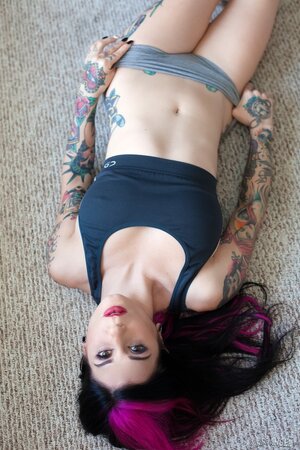 Tattooed woman poses in bedroom in lingerie that accentuates her assets