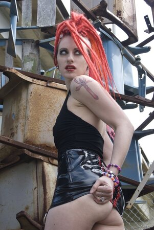 Tattooed emo girl with red dreadlocks poses naked in an industrial zone