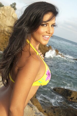 Ravishing brunette goes on rocky beach to pose under sun in yellow bikini