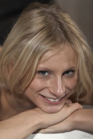 Skinny blonde Paris Pink smiles while posing nude on black leather couch