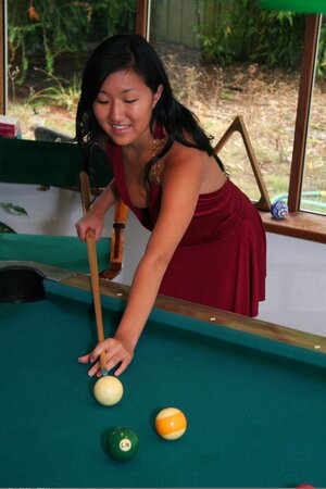 Asian babe in maroon dress climbs the pool table to pose without clothes