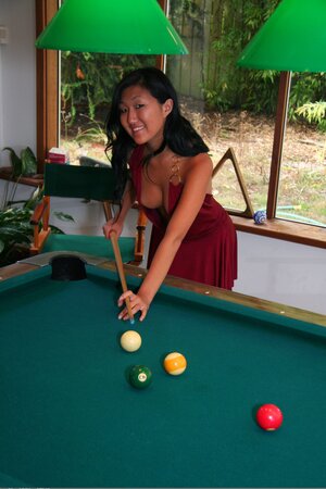 Asian babe in maroon dress climbs the pool table to pose without clothes