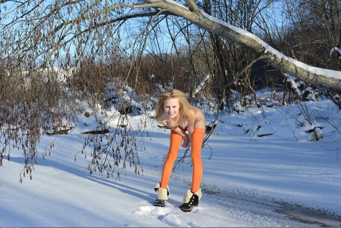 Young lady in orange stockings easily poses naked on a sunny winter day