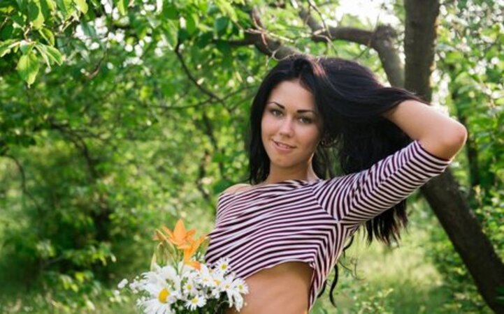 Raven-haired hussy with a bunch of flowers demonstrates her pussy in the woods
