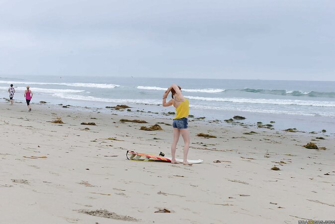 Redhead colleen in swimsuit is playfully posing with surfboard on the beach