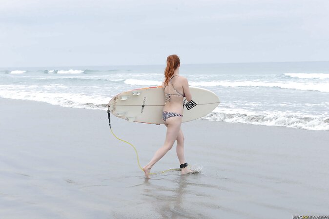 Redhead colleen in swimsuit is playfully posing with surfboard on the beach