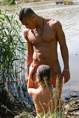 Chick in a cap banged by two dark-skinned boys on the grass by the river